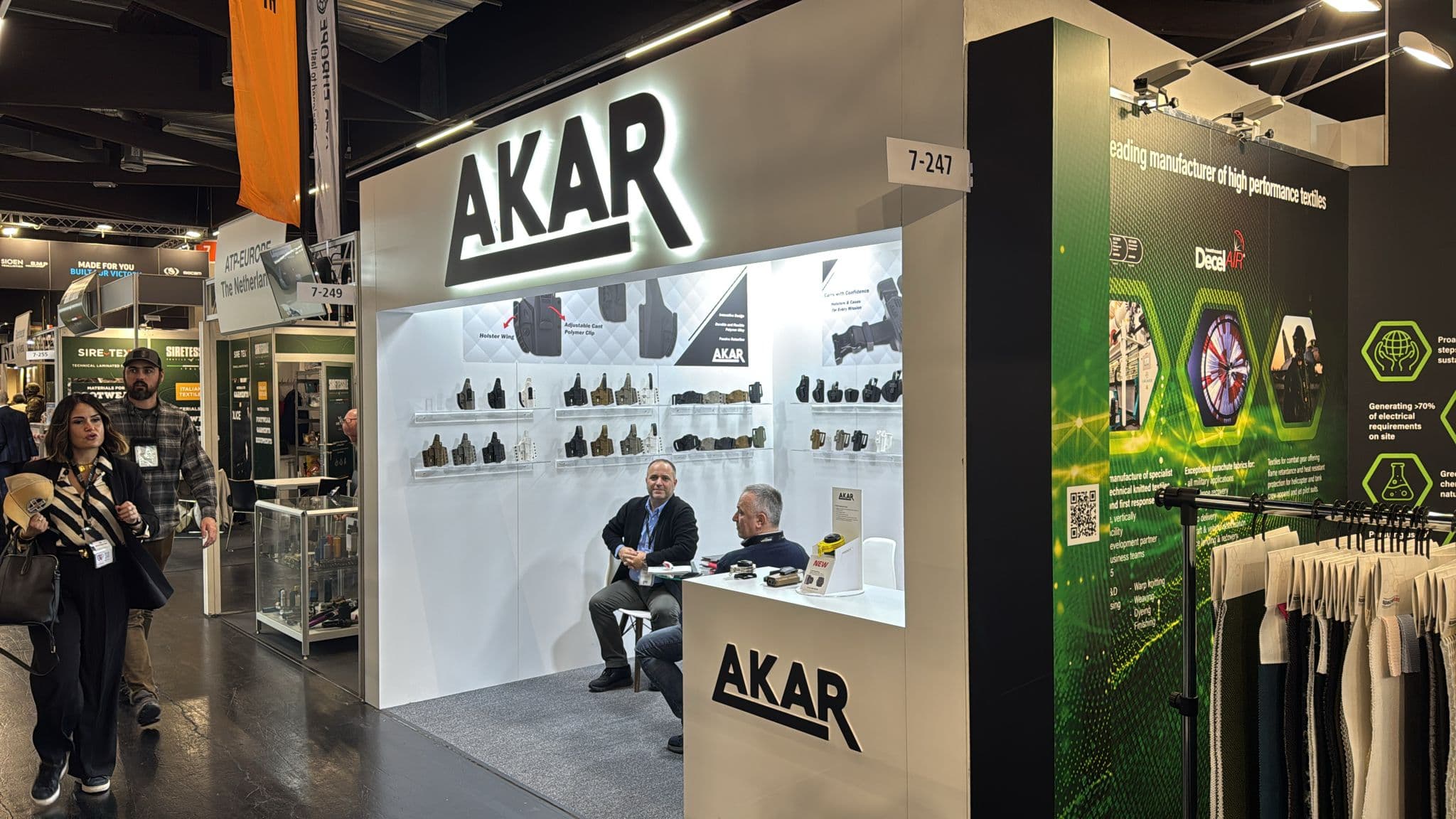 AKAR exhibition booth showcasing tactical holsters with staff seated inside at a trade show.
