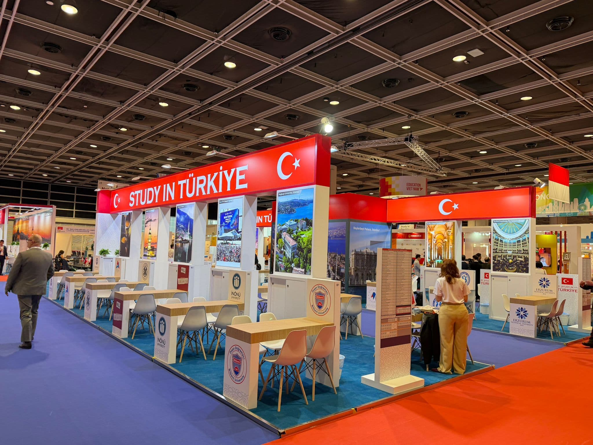 "Study in Türkiye" pavilion at an education fair with university information desks and seating.