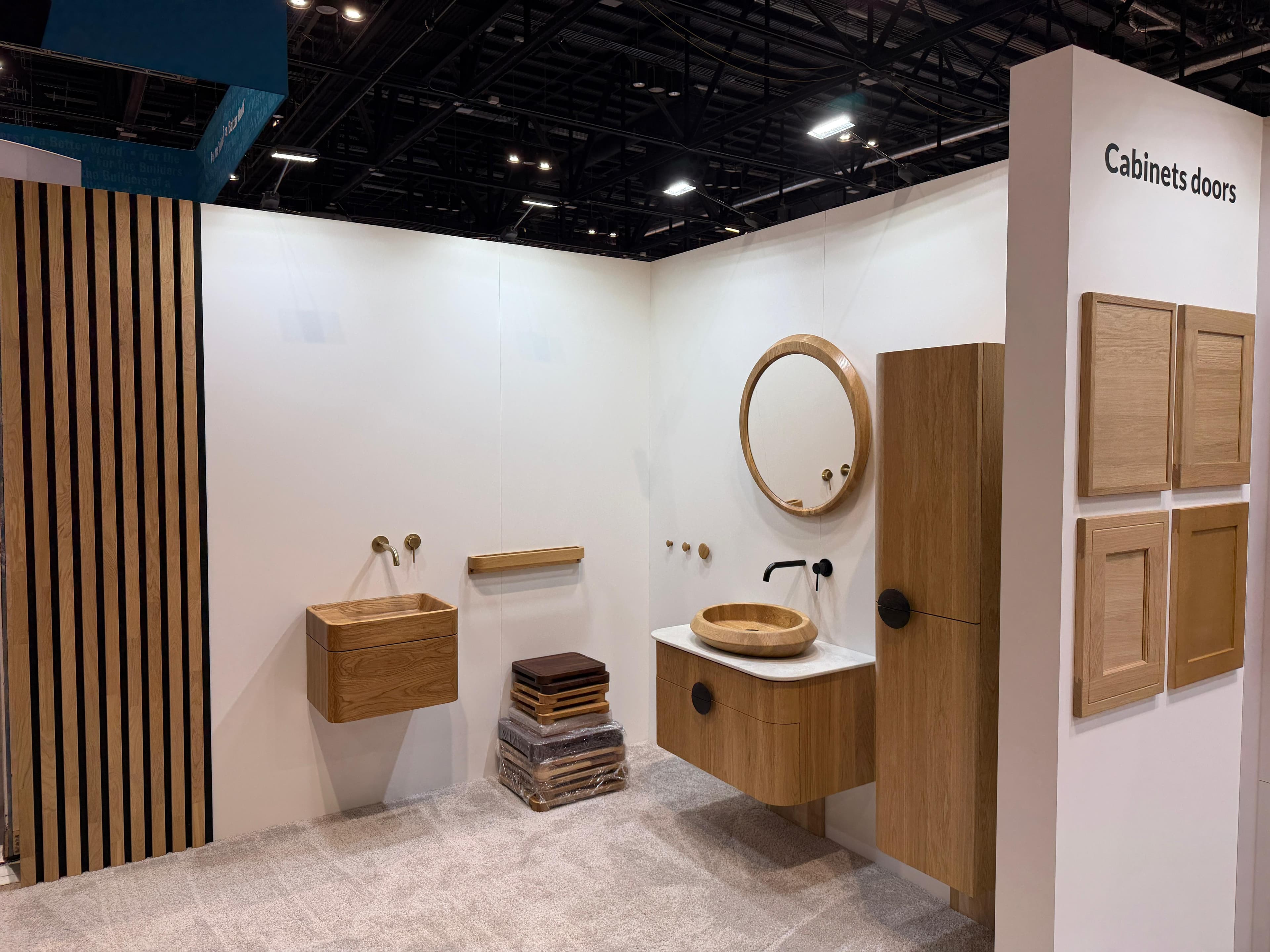 Minimalist showroom display of light wood bathroom vanities, vessel sinks, mirror, and tall cabinet.